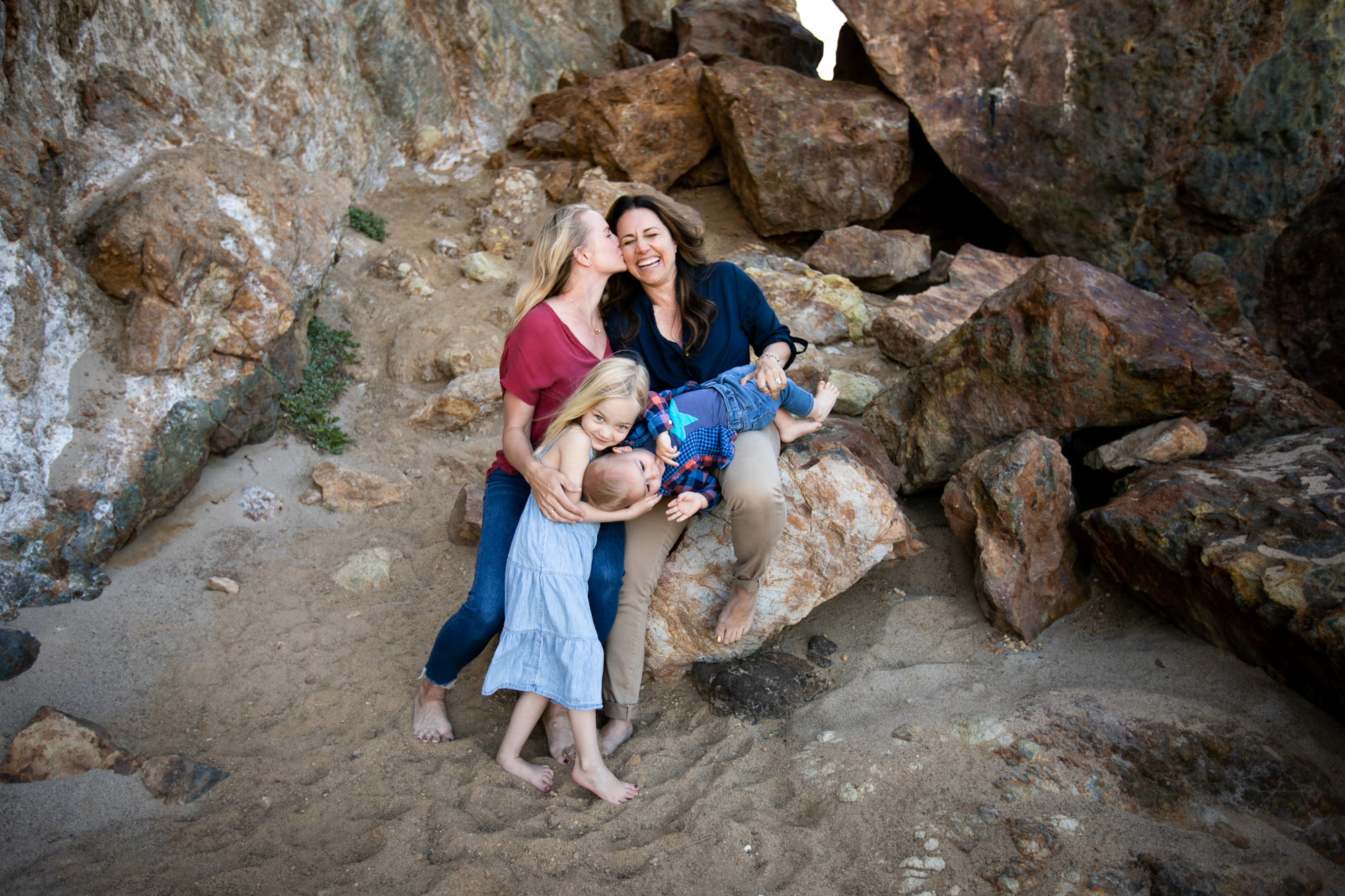 family poses on rocks at the beach in Malibu
